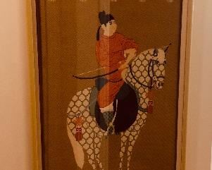 "Oriental Prince on Pinto Horse"; cross-stitched, tall image; prince in white and dark blue with horse filled with a traditional quatrefoil pierced screen pattern in blue-gray; on a rose pink field, with a navy blue panel at top an bottom; edged with cream color arabesques, Karmic knot hangers and tassels; signed LL corner: image: 68" h x 26.5" w; frame: 72" h x 30.5" w in a smooth laquer finish of dark cream color with corner insets of marled grays. $2,800 (Professional art appraisal in 2014 $18,000)