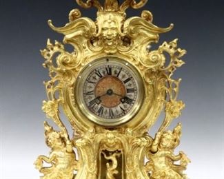 A turn of century Lenzkirch Bronze table clock.  14-day time and strike movement with Cast dial Silvered chapter ring and Roman numerals, original pendulum, serial #524962. Gilded Bronze  case with upper finial, mask and foliate design with cherubs and a Dolphin base with scrolled feet.  Very minor wear, flake in rear door glass, running when cataloged.  18" high.  ESTIMATE $1,000-1,500