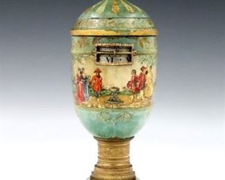 An early 20th century Annular mantle clock by Harold Carter-Bowles, Cheltenham, England 1889-1961.  8-day time and strike movement with rotating Silvered indicator rings having Roman numerals on hours and Arabic minutes.  Urn form turned wooden case with chased Bronze fittings, having a lift off cover, decorated with hand painted Court scenes.  Stamped mark "Carter Bowles, Cheltenham" under base.  Some paint wear, running when cataloged.  12 1/2" high.  ESTIMATE $1,000-2,000