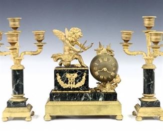 A diminutive turn of the century French three piece clock set.  Includes a Gilded Bronze and Verde Marble clock with a pair matching candelabra.  30 hour time only movement with platform escapement within a globe with Roman numerals and serpent hands.  The clock with a gilded Cupid figure with Bow and Arrow in hand beside the clock with love bird finial, on a Marble base with floral swag and a Bronze molding on flattened ball feet, en suite with two, three branch candelabra with engine turned candle cups, three foliate arms and matching bases.  Minor wear, running when cataloged.  Up to 10 1/2" high overall.  ESTIMATE $800-1,200 