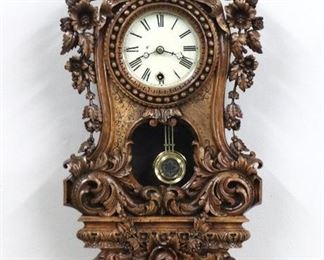 A late 19th century carved German wall clock by Philip Haas & Sohne.  8-day spring driven time only movement with painted metal dial and Roman numerals.  Carved  Walnut case with urn finial and the motto "Benutze die Zeit" or "Seize the Time", above a beaded bezel flanked by floral detail and a foliate and scrolled lower door.  Refinished with minor wear, replaced minute hand, running when cataloged.  25" high.  ESTIMATE $600-800