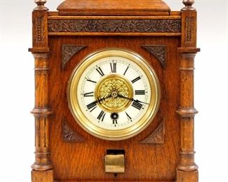A turn of the century Hotel Master alarm clock.  8-day time only movement with platform escapement, porcelain chapter ring with Roman numerals and embossed Brass center.  Upper multi slot index dial with 15 minute increments and Brass tablets under a hinged cover.  Oak case with applied composition decorations.  Older finish with minor wear, dial hairline, added 9 volt alarm bell, running when cataloged.  13" high.  ESTIMATE $400-600
