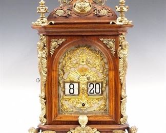 A late 19th century Lenzkirch Digital Bracket clock, retailed by "G. Landmann & Co., Frankfurt a M (am Main)".  The digital or "flip" clock was conceived by the Austrian inventor and engineer Josef Pallweber in 1890 and produced by the world-renowned Lenzkirch Clock Factory between 1893-1894.  This clock features an 8-day time only movement with Silvered dial and Gilded Bronze Apollo mask decoration, serial # 1 Million 2895 (1893).  Figured Walnut case with shingled "roof", cast Bronze finials and mounts, single door with arched beveled glass and Bronze Cherub columns on a molded base with winged figural feet.  Older finish with good color and only minor wear, small loss to rear door panel, running when cataloged.  25" high.  ESTIMATE $8,000-12,000