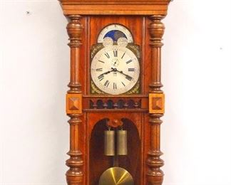 A turn of the century Gustav Becker wall clock.  8-day weight driven time and strike movement, arched Silvered dial with Roman numerals, Brass spandrels, painted Moon phase in arch with subsidiary seconds and date aperture, serial # 1588882.  Altdeutsch style Walnut case with arched crest, carved finial and foliage over a single long door with arched dial glass and shaped lower flanked by turned pilasters with fluted detail over a shaped lower drop with turned finial.  Older finish with some wear, restored crest finials and drop, running when cataloged.  58" high.  ESTIMATE $400-600