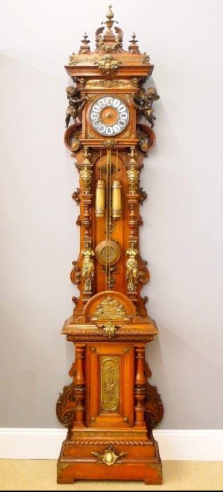 A Good 19th century German hall clock, attributed to Lorenz Furtwangler & Sohne.  8-day weight driven time and strike movement, Cloisonne dial with Roman numerals, Oak center and cast Bronze inner bezels, embossed brass pendulum bob and matching Cloisonne weights.  Carved Oak open well case with high quality Bronze mounts throughout features a shaped crest with Bronze finials and swags over molded cornice with Bronze frieze and masks an open dial with molded Brass bezel flanked by full bodied Bronze cherubs over the open well with arched backboard and applied bronze decoration flanked by turned columns with Bronze caryatid bases and scrolled sides, on a paneled base with arched bronze mounted crest, Bronzes allegorical panel flanked by turned columns with Bronze rings on a stepped plinth with gadrooned and molded transitions and simple block feet.  Old finish with wear some repair and minor damage, running when cataloged.  102 1/2" high, ESTIMATE $8,000-12,000
