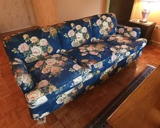 This sofa is on wheels and is a white sofa that is covered in the floral print. 