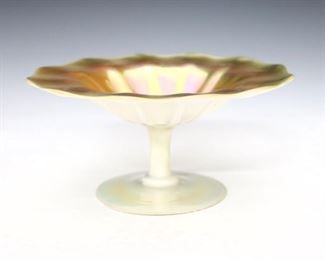 An early 20th century Steuben glass compote with Gold Aurene interior and Calcite exterior. Shape #2760, round form with ribbed bowl and scalloped rim on a pedestal base. Polished pontil with original "Steuben" Gold foil sticker. Minor surface wear. 6" diameter and 3" high. ESTIMATE $200-300