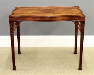 A Baker Chippendale style silver table. Mahogany construction with bookmatched shaped top and molded edge over a conforming skirt and tall molded legs with pierced corner brackets and flared feet. Original "Faded" finish with slight wear and minor surface imperfections. 34 1/2 x 22 1/2 x 27 1/2" high. ESTIMATE $400-600