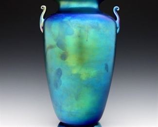An early 20th century Steuben Blue Aurene Art Glass vase.  Shape #6630, footed urn form with flared rim and two scrolled handles.   Un-polished pontil with etched "Steuben Aurene" and shape "6630".  Minor surface wear with 3/4" long scratch at lower body.  12" high.  ESTIMATE $800-1,200