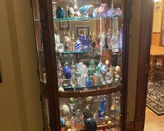 Curio cabinet filled with decorative eggs, paper weights and perfume bottles