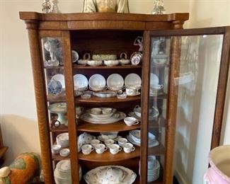 Oak bow-front, claw-foot china cabinet filled with beautiful porcelain and hand-painted Limoges pieces.
