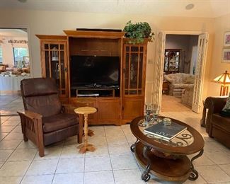 Looking across the den and showing the Arts and Craft style leather recliner, two pedestal tables, modern oval coffee table with glass top and metal legs, Arts and Craft style entertainment center