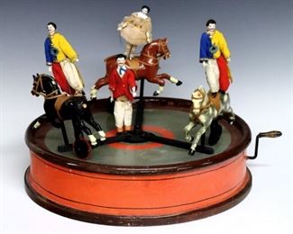 An early 20th century child's toy circus.  Three carved wooden horses with acrobats and ring master on a Paper Mache base with hand-crank mechanism and internal music box.  Includes an extra horse.  Wear and some losses, lacks horse tails.  16" diameter x 13" high.  ESTIMATE $200-400