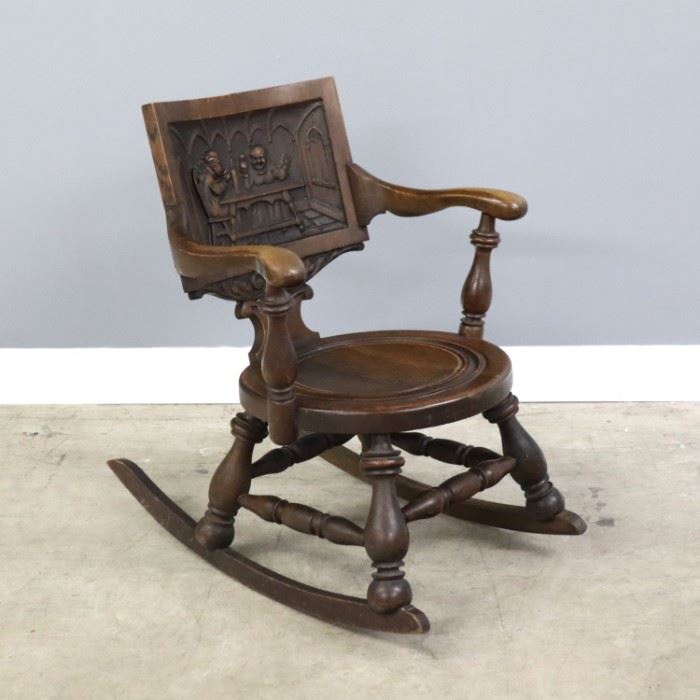 A late 19th century American rocking chair.  Oak construction with carved tavern scene in back, scrolled arms with turned supports, circular seat with turned design on a heavy turned stretcher base with shaped rockers.  Original finish with wear, joint separation to seat.  20 1/2 x 30 x 31 1/2" high overall.  ESTIMATE $100-150