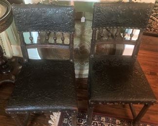 Two of four embossed leather chairs with brass atop the back