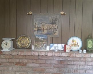 Living Room Fireplace Mantel Decorations: Decorative French Embroidery. Vintage Scale. Mexican Souvenir Plate. California Wine Book. Small Frames. Decorative Plate, Vintage Green Clock. Christmas Mug and Collectibles.