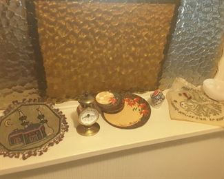 Travel Collectibles on Hallway Ledge. Beaded Doily from Jerusalem, West Germany Small Clock. Coasters from Romania. Small beaded Egg. Alabaster Small Bowl. Small Shot Glass. Embroidered Doily from Greece.