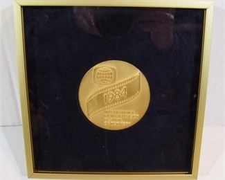 2577   1984 Bronze Medallion from the International Film & Television Festival of New York, 2 5/8” dia., mounted in a metal frame, 7” sq.  Note:  Back of medallion is un-engraved, back of frame inscribed “Shirley Eder”. Cond: No damage found, medallion loose in interior.