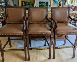 Three Leather Barstools by Hancock and Moore. Beautiful curved arms and rivet detailing! There are some light scratches, but all are in otherwise great condition. Each measure 21” wide, 18” deep, 29” high to the seat and 44” high to the chair back.