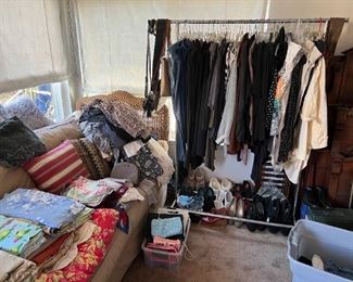 Clothing on the rack, blankets and pillows on the sofa, and shoes below the clothes.