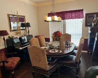 The formal dining room with a beautiful oval dining table with beautiful inlay and six high back upholstered chairs, Yamaha Piano in silk ebony, Royal Doulton china and beautiful table linens and hides