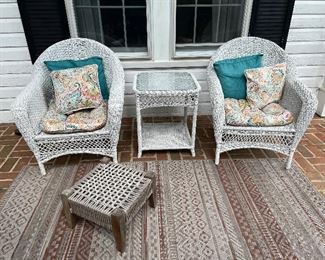 2 white outdoor wicker armchairs with matching center table and woven ottoman atop an outdoor patterned rug