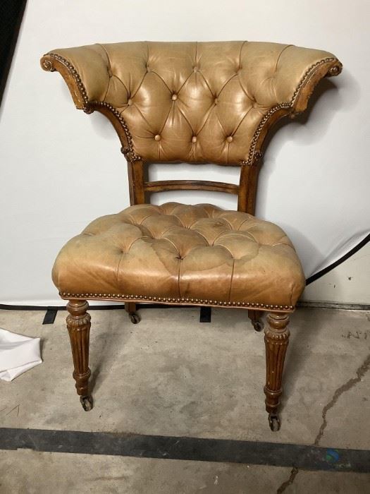 Vintage chair with taupe leather-like fabric, rivets, and buttons, carved wood frame with legs on wheels, wood has some nicks and scratches and fabric shows some staining, H 37" x W 30" x D 25".