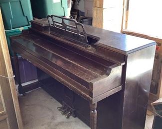 Vintage Baker Newark dark wood piano with brass colored pedals. Surface shows scratches and scuffs indicative of age and use, (1) knob on key cover is missing, Music sheet tray appears to be loose, (1) white tile on one of the keys is missing, H 36" x W 53" x D 24".