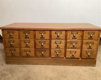 Appears to be solid oak 18-drawer library card catalogue file cabinet. Some drawers have metal or wood centerpieces, H 17"x W 39.5"x D 17", with wear marks and scuffs on top surface, sides and corners. Top comes off of base.