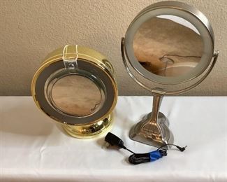 Includes a silver colored by Zadro, H 16" x W 10" x D 6", and a gold colored mirror by The Sharper Image H 12.5" x W 9" x D 8" (had additional smaller mirror hung overtop), both are in unknown working condition.