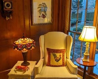 Comfy upholstered armchair, white wooden side table, vintage stained glass table lamp, MCM side table, w/vintage Italian table lamp, w/shade, finial, vintage Belgian wall clock and nicely framed/matted botanical.