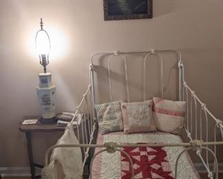Cast iron child's bed with a number of small vintage an antique quilts with a darling oil painting of owl above the bed.