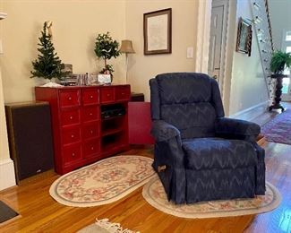 Blue La-Z-Boy recliner,  Two hand hooked oval wool rugs, two JVC speakers, multipurpose wood cabinet,  symphonic video cassette recorder and DVD CD player, CDs, DVDs, Christmas tree, Christmas topiary, decorative lamp, needlepoint picture...