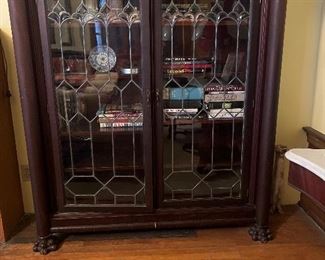 Empire Style mahogany veneered bookcase. Rectangular top with projected molded cornice over conforming frieze above a pair of slightly arched geometric leaded glass cupboard doors enclosing four shelves, flanked by engaged columns with Corinthian capitals, set on paw feet. American. Heights 61 1/2", Width 55 1/2", Depth 18".