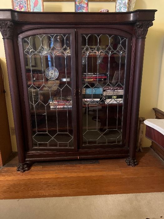 Empire Style mahogany veneered bookcase. Rectangular top with projected molded cornice over conforming frieze above a pair of slightly arched geometric leaded glass cupboard doors enclosing four shelves, flanked by engaged columns with Corinthian capitals, set on paw feet. American. Heights 61 1/2", Width 55 1/2", Depth 18".