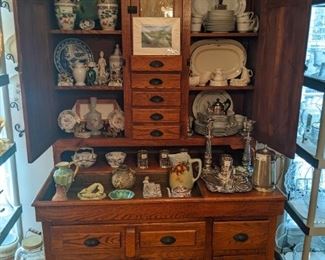 Close-up of the vintage oak display cabinet, w/ slag glass and collection of Asian porcelain vases, English silverplate, hotel silverplate, hand-painted ceramics, blue/white Asian porcelain charger, collection of glazed saltware pitchers and 36-piece set of Wyndham "Harmony" china, Japan.