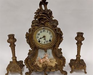ANTIQUE ANSONIA ROCOCO STYLE METAL MANTLE CLOCK. HAS PLAQUE WITH CHERUBS ON THE FRONT. 14" TALL. INCLUDES PAIR OF NON- MATCHING CANDLE STICKS.
