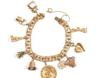 Lot 119  |  GOLD CHARM BRACELET  |  A 14k gold chain bracelet (pat 3308517) with mostly 14k charms, including: an articulating sewing machine and table, a wishing well with articulating pail, a windmill, a green enameled Christmas tree, a pearl & gold bell, a cupid charm, a basket with enameled flowers, a heart with a single melee diamond, the statue of liberty, and a monogram charm; total weight 49.4g
