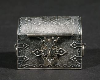 Lot 193  |  MINIATURE STERLING SILVER ARMORIAL CASKET  |  Small cloth-lined casket with armorial decorated lid, showing a cross in a shield crested by a crown and flanked by two lions, with articulating side handles
h. 1-1/4 w. 1-3/4 in.
