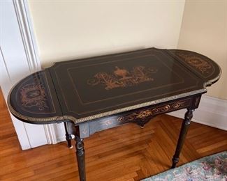 Black lacquer games table with intricate decorative inlay, brass trim, and side drop leaves