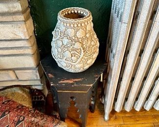 Unusual carved Asian vase sitting on a wood plant stand.