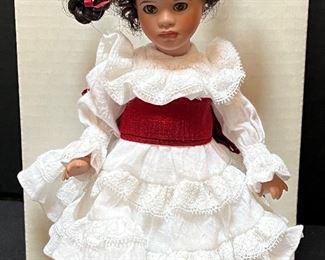 Merely Me Collection Doll Precisely Paloma. A lovely doll by California doll artist, Wendy Lawton. Her name is Precisely Paloma and she is #67 out of 250 dolls made and is from the Merely Me Collection from 2002. She is 9” with a porcelain head and hands on a spring jointed wooden jointed body. She has pretty dark brown hair tied in two braids that stick out, brown glass eyes, and is wearing a lovely white cotton and lace dress made to twirl as she heads to the fiesta dance. The dress has a red silk tie around the waist. She has on white panties, long white socks, a white slip, and dark red leather tie shoes
Number 67/250.