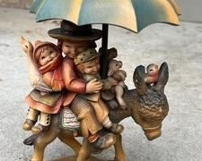 Anri Figurine Riding Through the Rain. Measures 10.5" h. Has some light wear including some slight paint loss on the donkey's ears and umbrella.