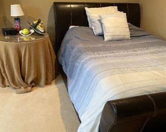 Queen faux leather sleigh bed, skirted side table with glass top, and pistons table lamp