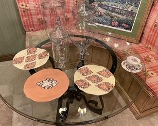 Glass-topped round table with black metal base, shown with ceramic serving plates and 3 large glass urns
