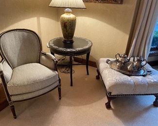 Upholstered armchair, hand-painted side table, ceramic table lamp, tufted ottoman with nail-head trim, and silverplated coffee/tea set, and silverplated tray