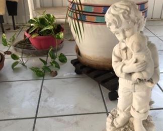 Resin yard ornament boy holding puppy. Ceramic pot with palm plant.