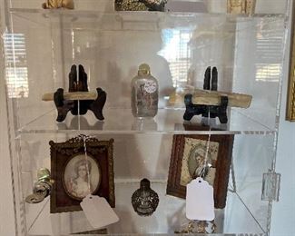 Living Room:  A Lucite display case shows a Netsuke horse;  a Radha Krishna painting on a tile; a carved figure; two pieces of scrimshaw; a painted glass snuff bottle; a small perfume bottle; and several framed miniature portraits.