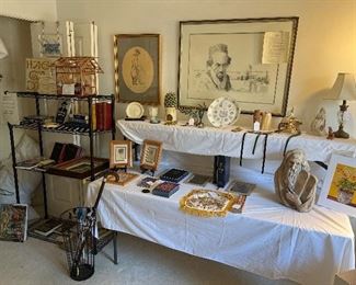 Bedroom #2:  A black metal rack displays numerous books and a wooden bird cage.  The table displays a variety of items including small prints, TORAHs, decorative masks, a MOSES figure, and more. 