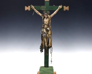 A turn of the century Latin American carved wood Crucifix.  Depicts a crucified Christ in woven garments and polychrome decoration.  Added adornments including embossed tin pins, a miniature portrait and rosary.  Some wear and minor damage, touch-ups to cross.  12" high.  ESTIMATE $300-400
